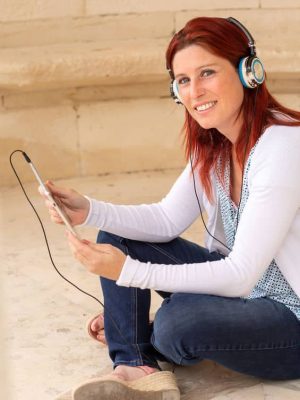 Pretty smiling redhead woman sitting on the floor listening to music or watching a movie on a touch pad